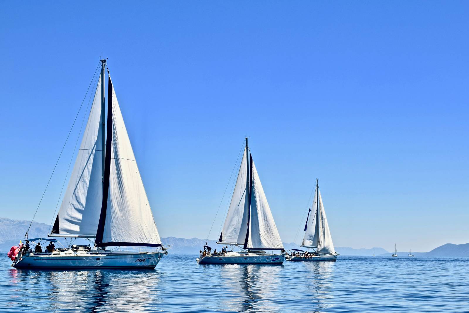 3 sailboats sailing in a convoy with a clear sky in the background.