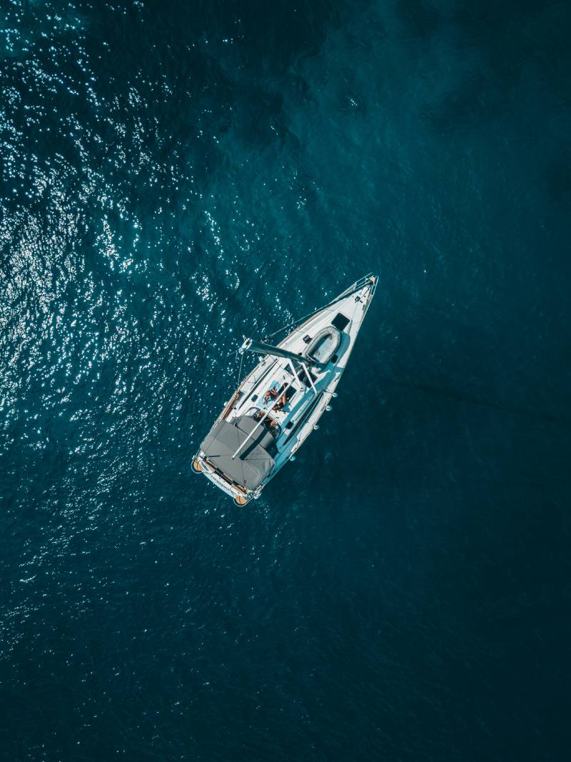 Medium sized sailboat with it's sails down photographed from directly above in a dark ocean.